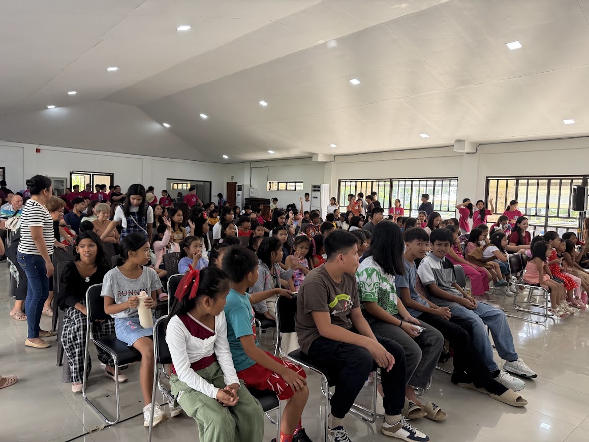 The hall fills — children in the front rows, families settling in behind.