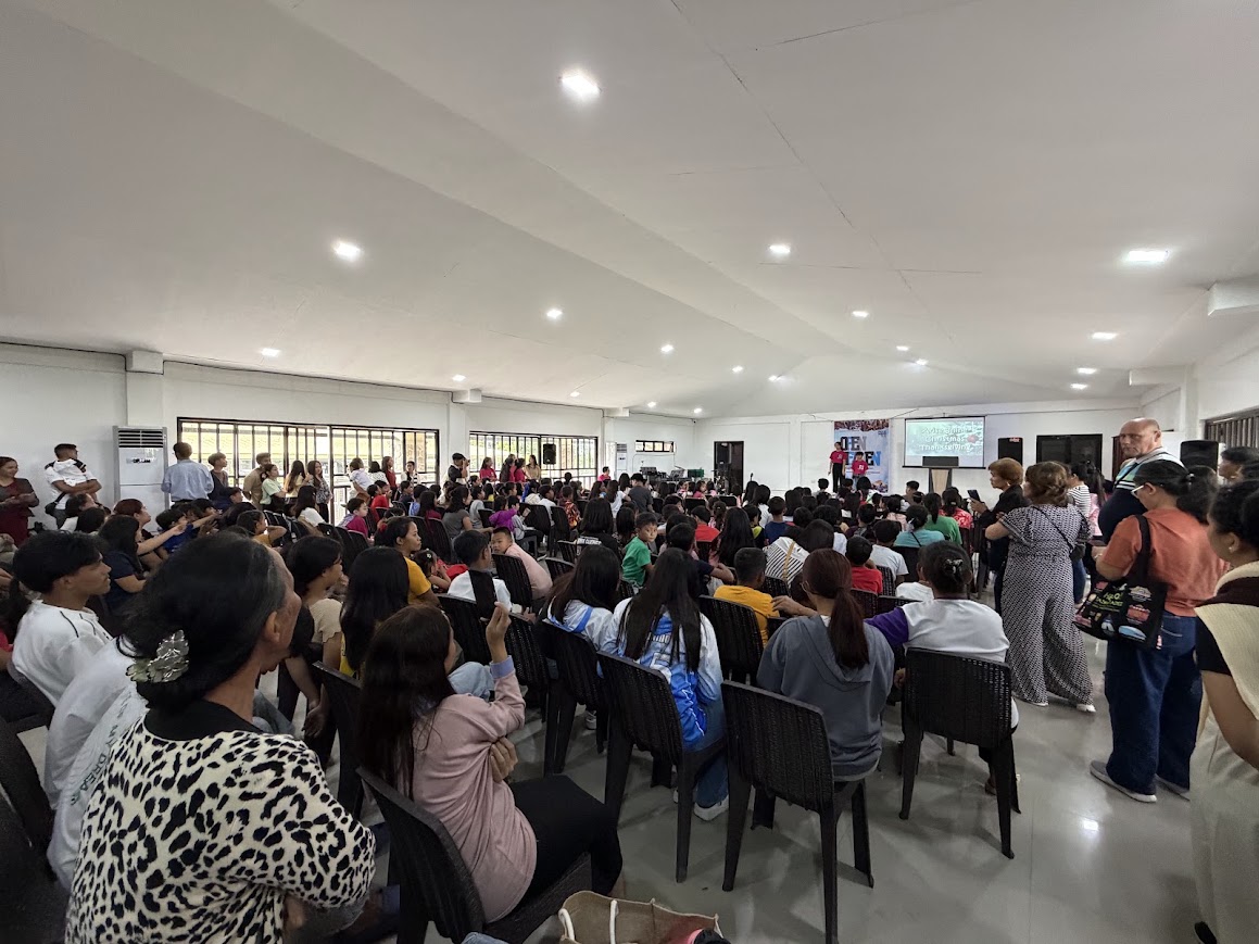 The crowd seated, the team at the front, families along the sides.