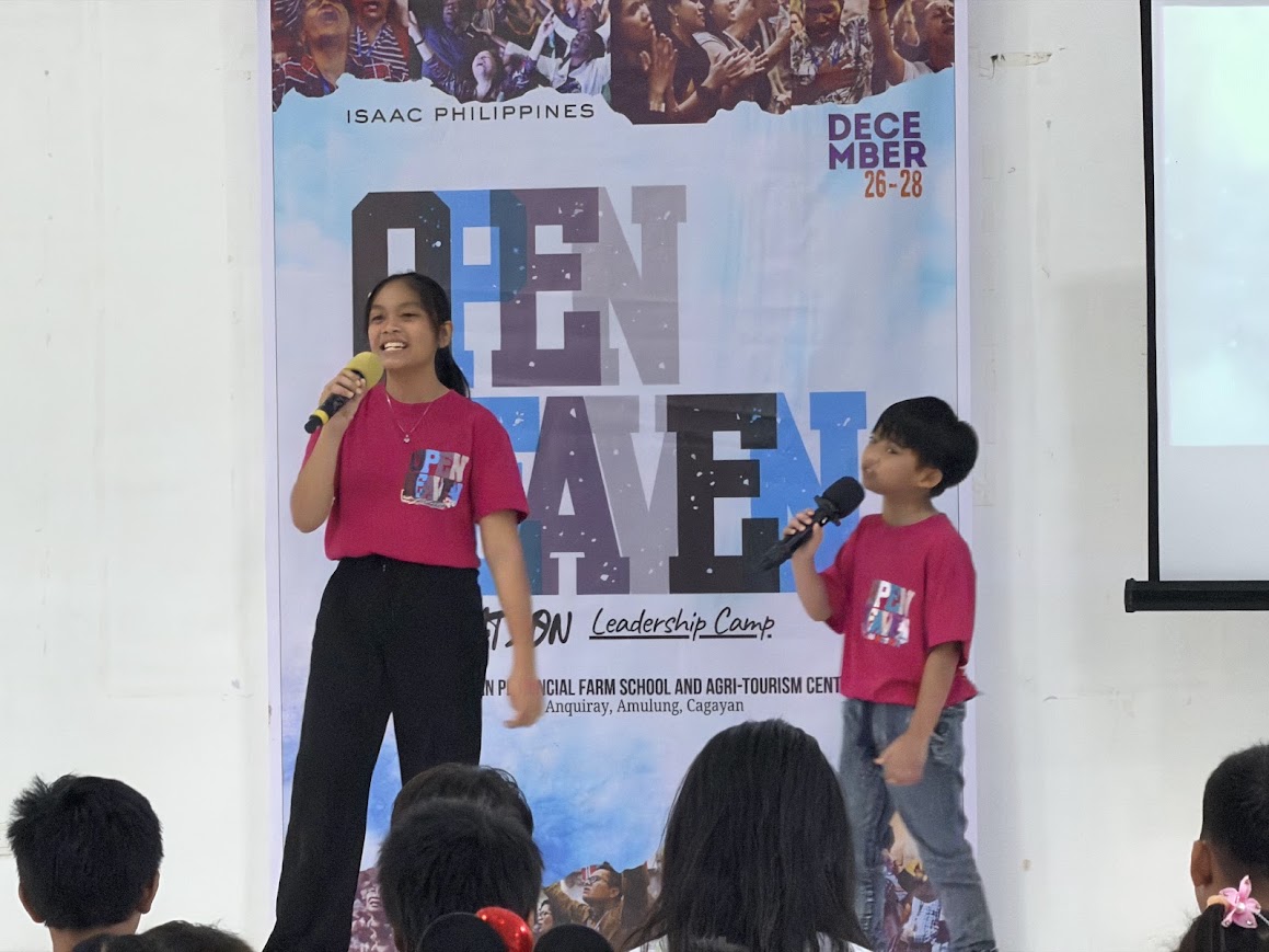 A youth duet at the mic in front of the Open Heaven banner.