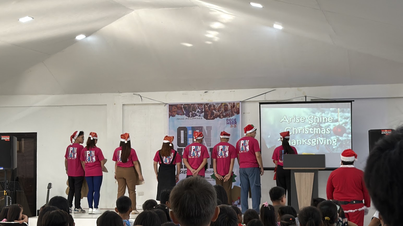 The skit cast lines up on stage with their backs to the crowd, Santa at the podium.