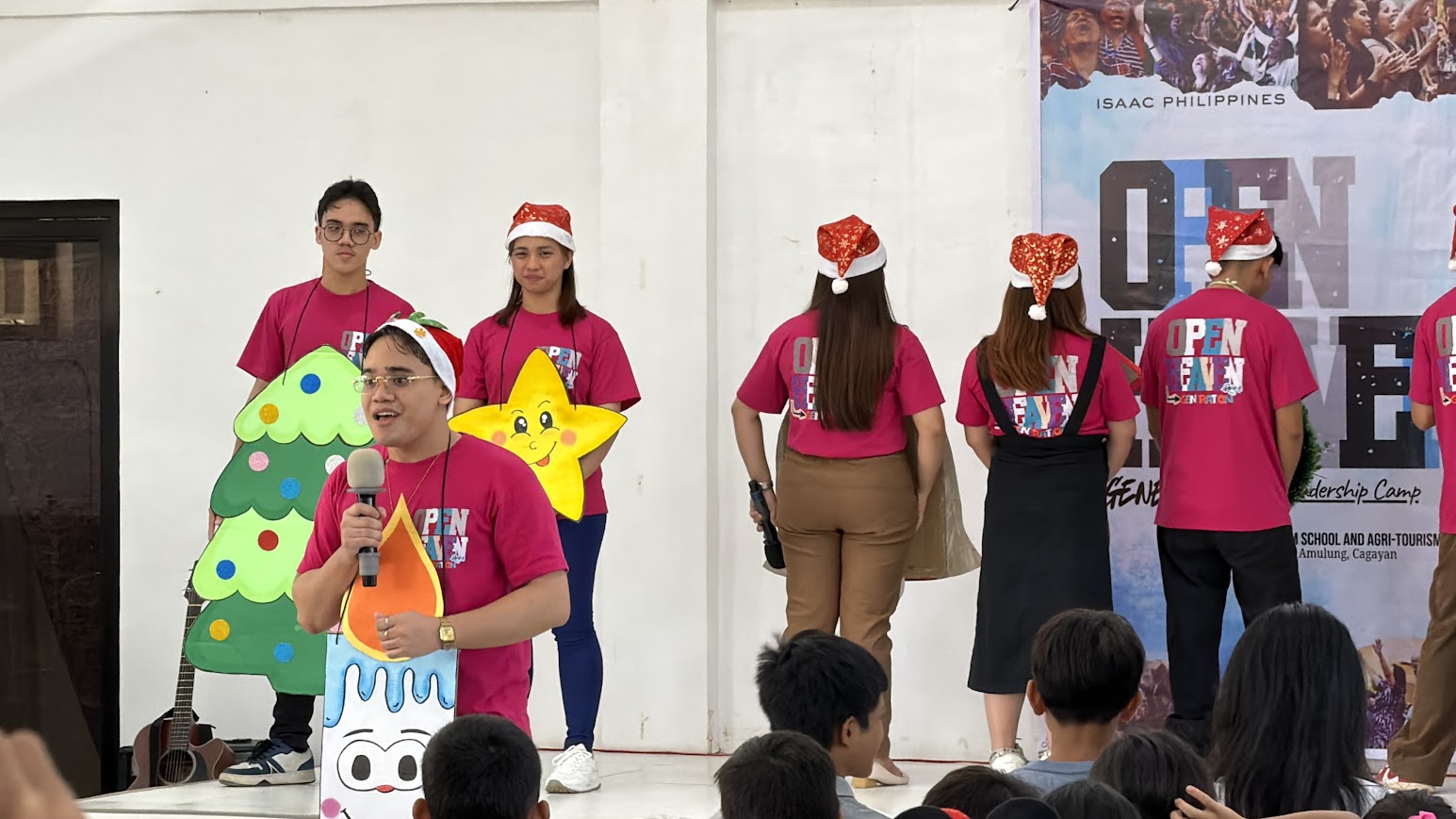 A narrator with a candle prop speaks, the tree and star behind.
