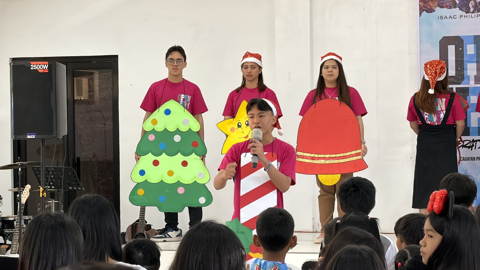 The candy cane takes the mic, the tree and bell behind.