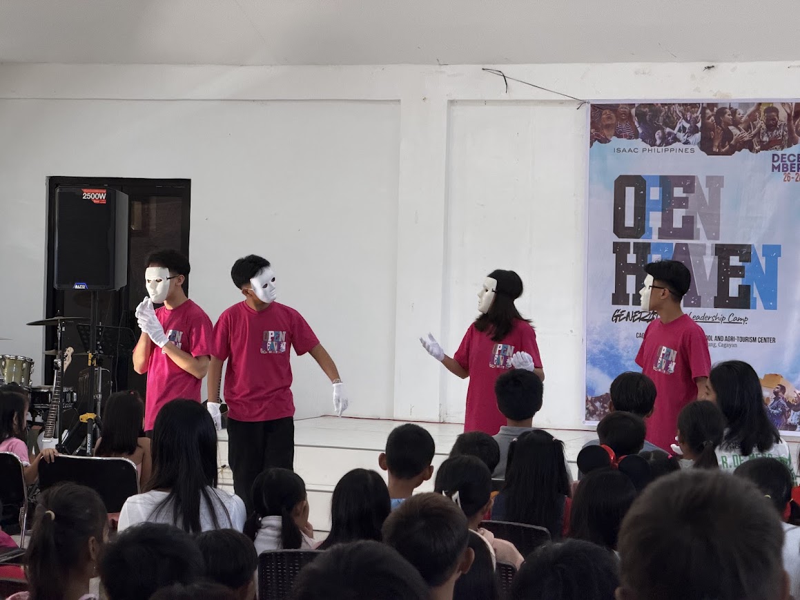 The masked mime — four performers in white masks and gloves on stage.