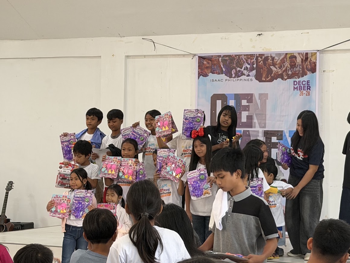 Children hold up their gift packs in front of the banner.