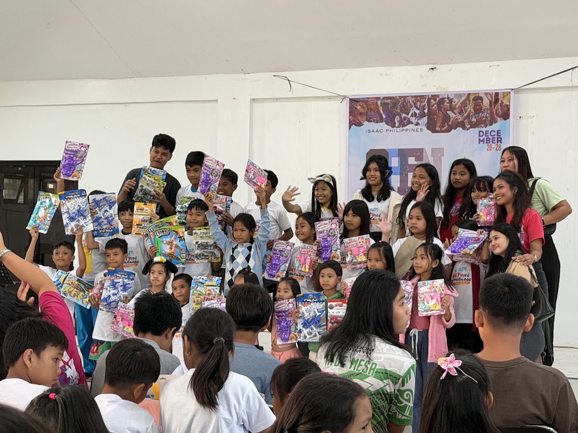 A larger group on stage with their gifts, volunteers at the sides.