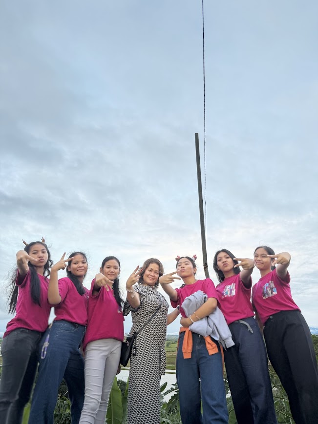 Six youth in Open Heaven shirts with a team member on the hillside, rice fields below.