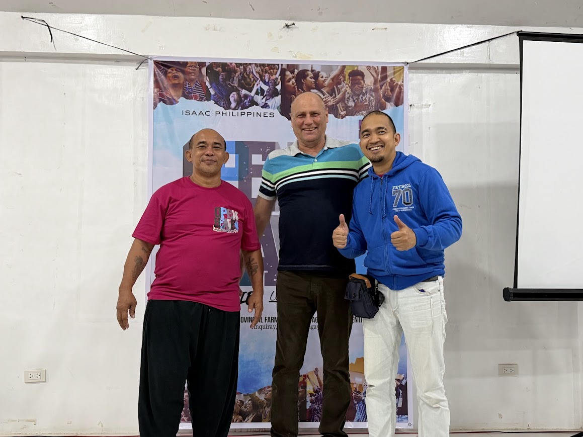 Three leaders in front of the ISAAC Philippines / Open Heaven banner, thumbs up.