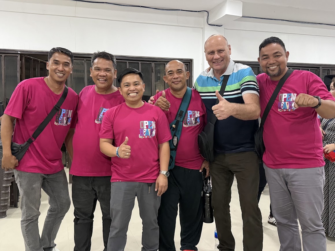 Six team members, five in Open Heaven shirts, thumbs up in the hall.