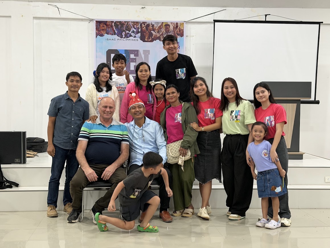 Team and family photo in front of the ISAAC Philippines / Open Heaven banner.