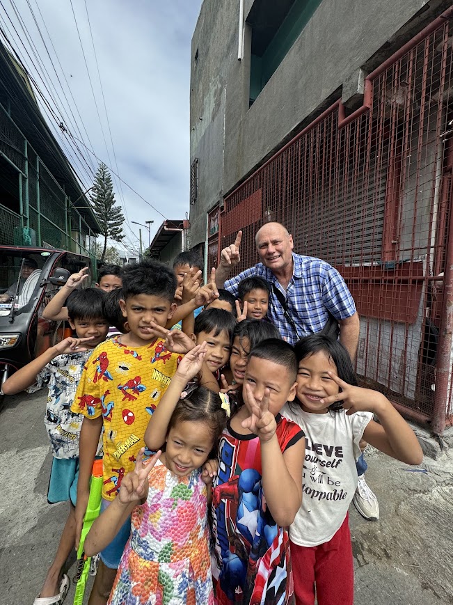 The day begins on the streets of Dasmariñas — a team member with a crowd of neighborhood children before the gathering.