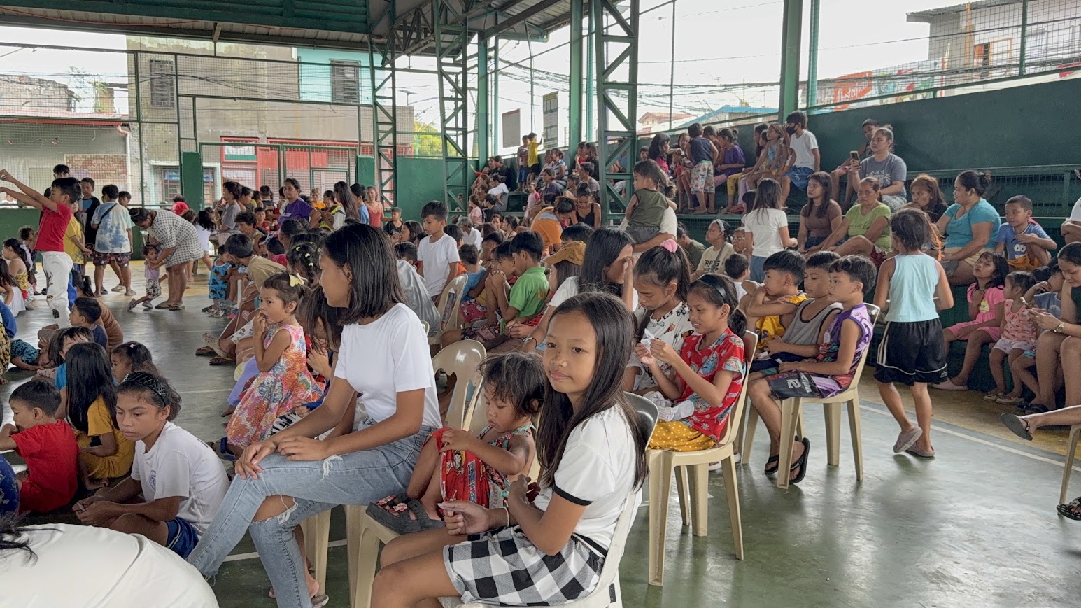 Children settle into the front rows, families taking their places in the stands.