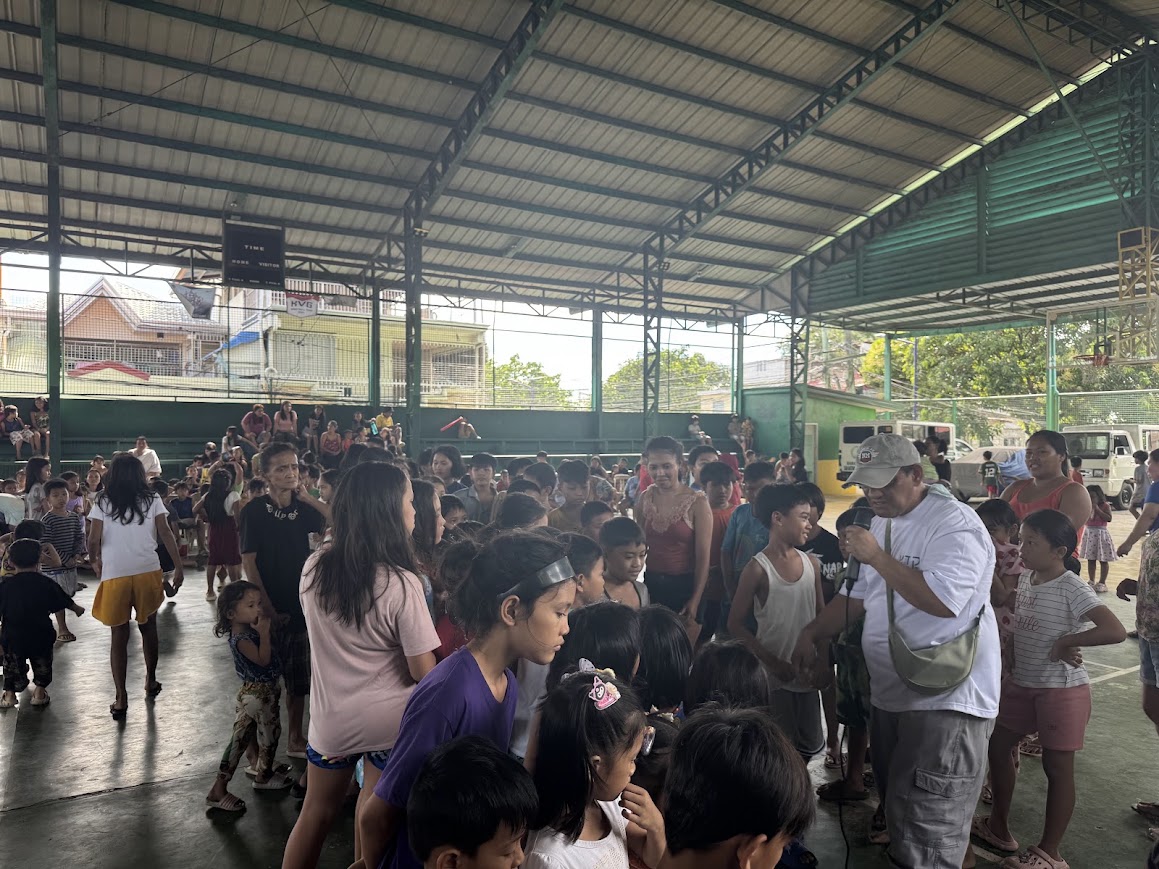 A team member with a microphone moves among the seated children.