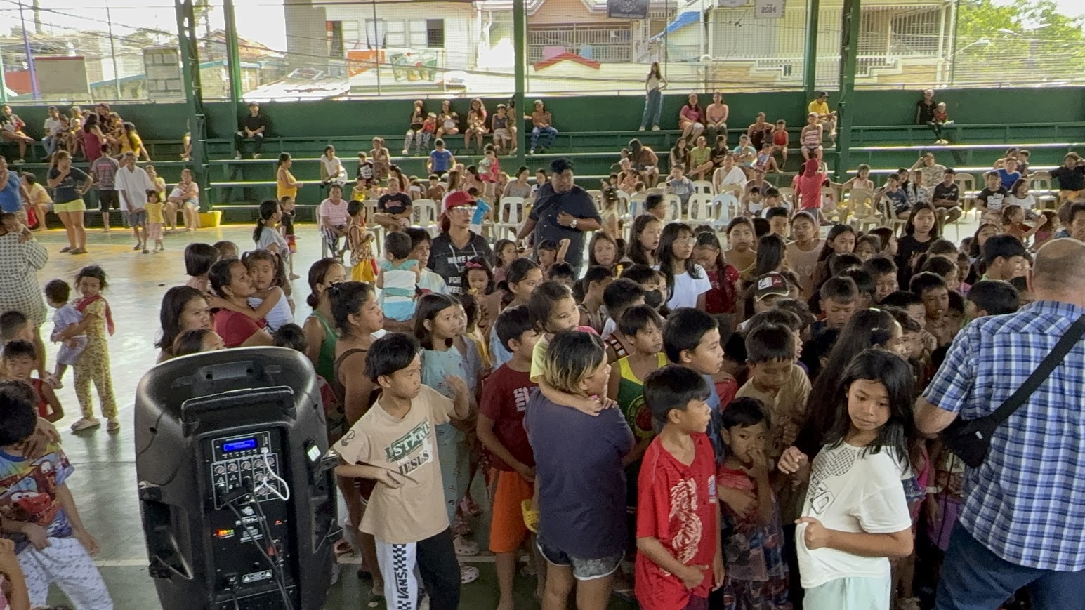 Seen from the back — the leader faces a court full of seated children.