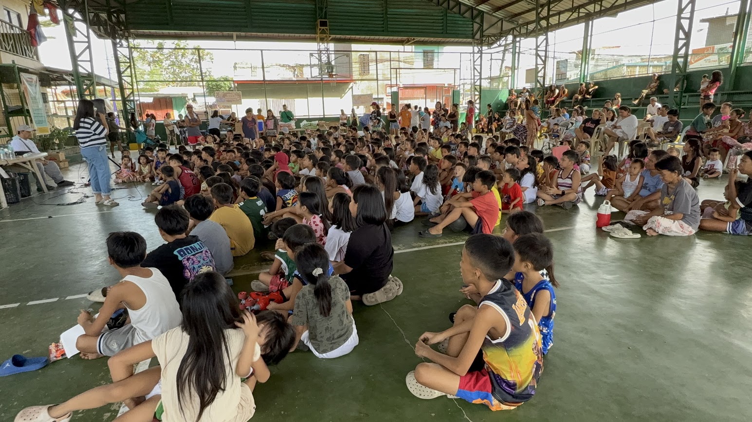 From the side — the leader speaks as the children raise their hands.