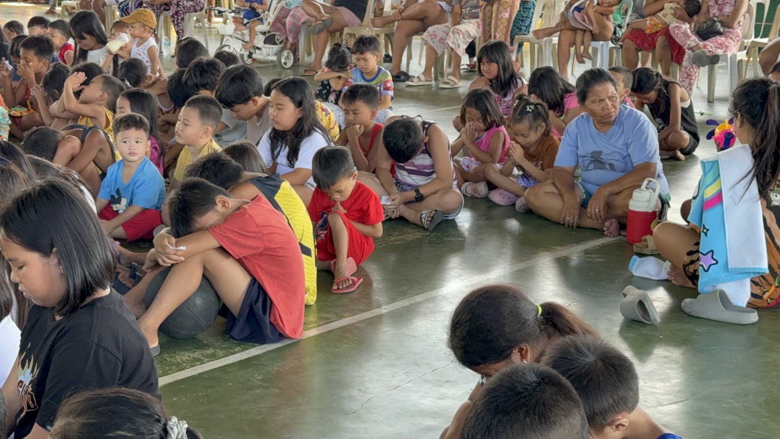 Heads bowed — one boy rests against a basketball as the crowd prays together.