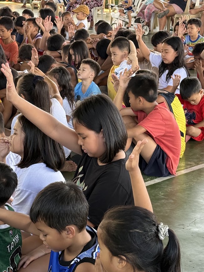 A young girl raises her hand beside a friend during the prayer.