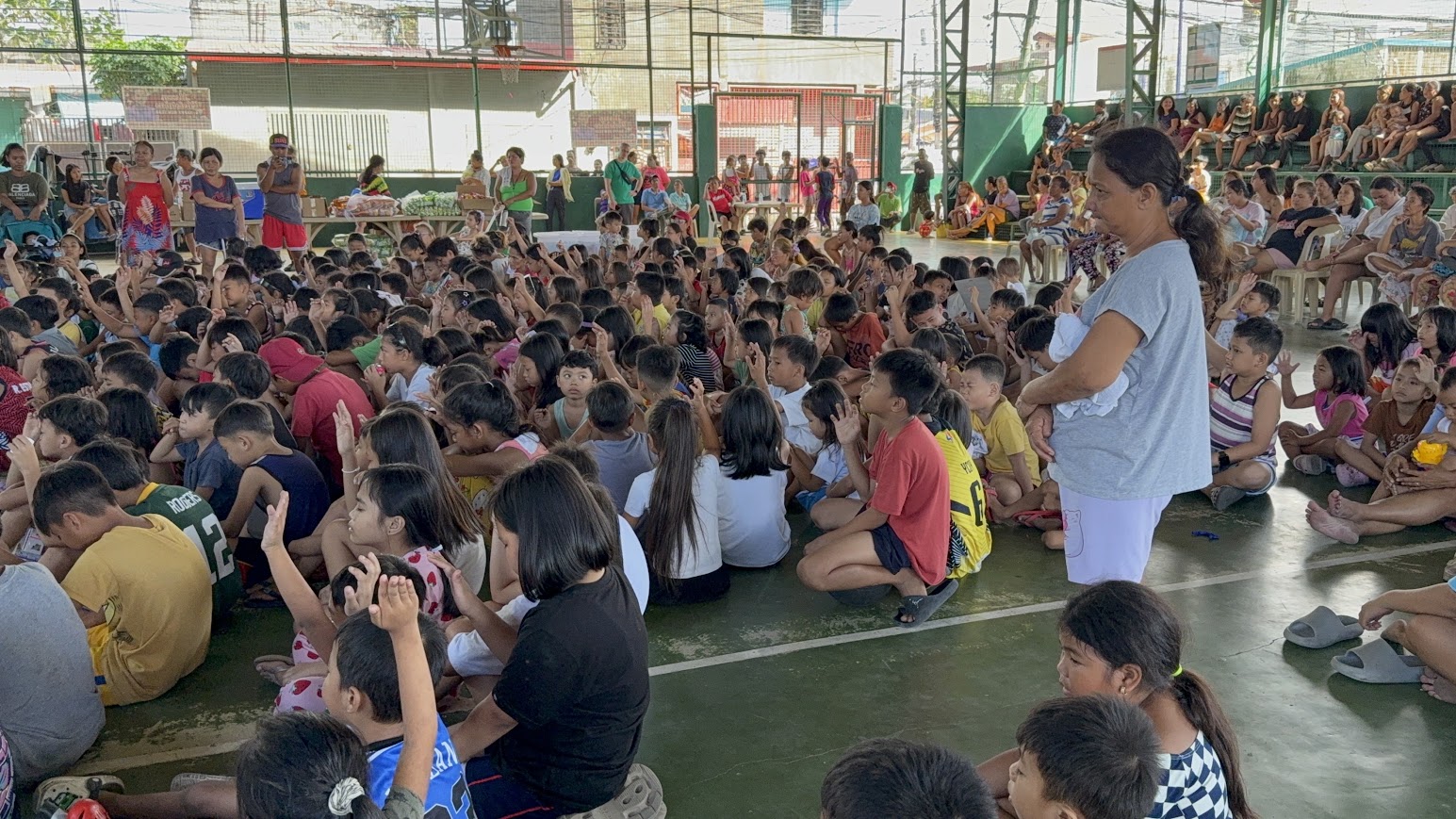A team member stands among the seated children as hands go up around her.