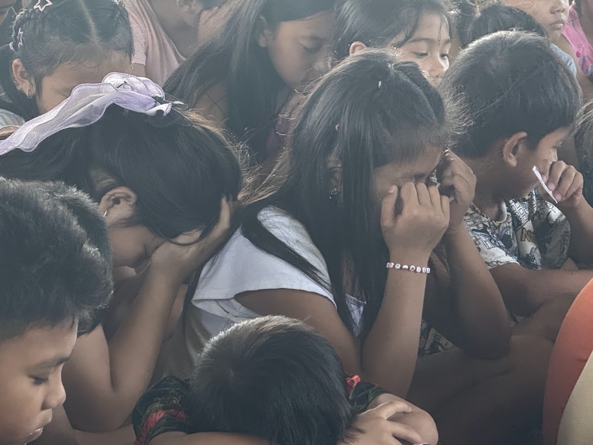 A cluster of girls, heads bowed and hands over their faces.