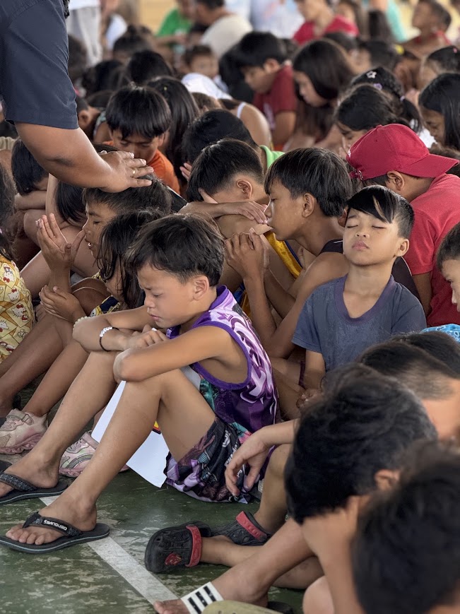 A team member's hand rests on a child's head during prayer.