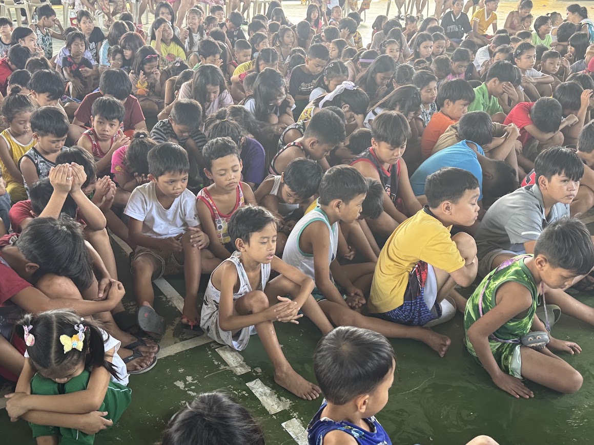 Rows of seated children, heads bowed.