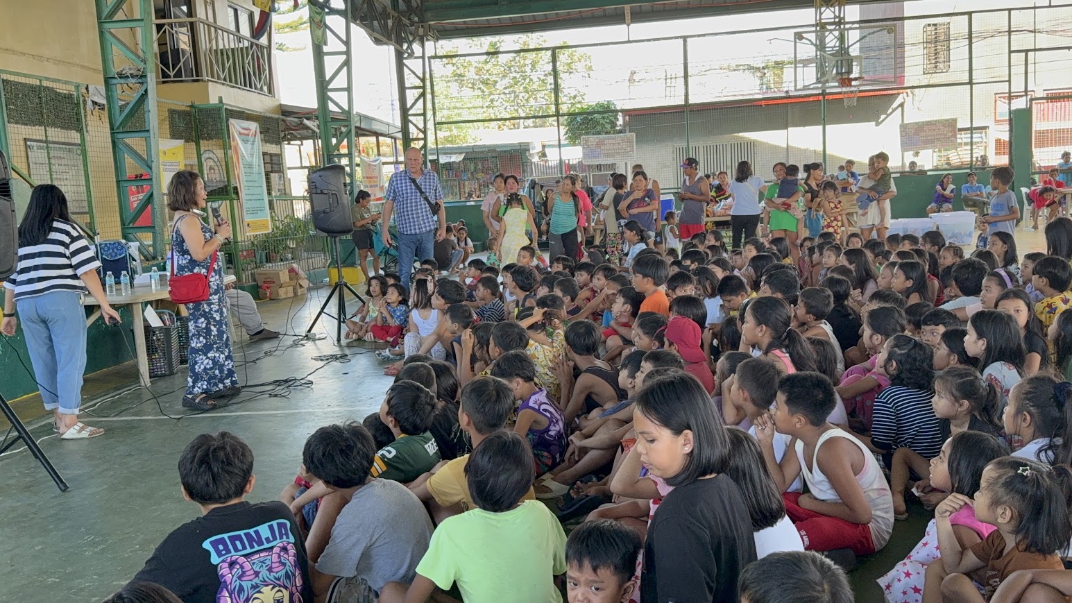 A team member in a floral dress addresses the children.