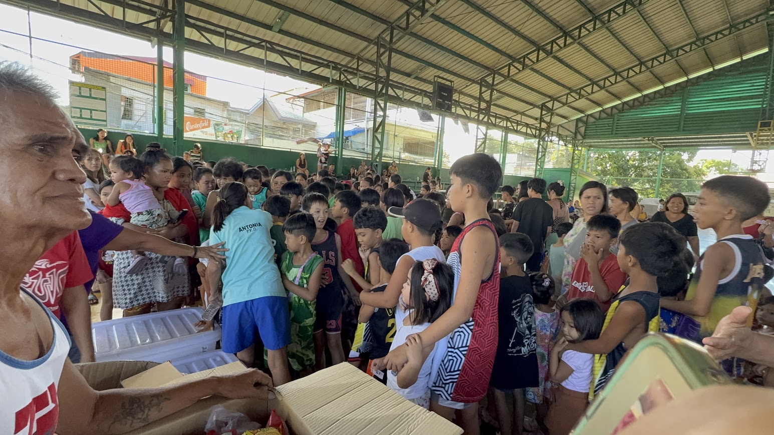 Distribution begins — children gather at the table as the coolers open.