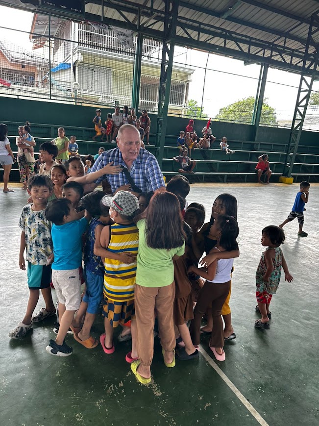 A team member caught in a group hug from a crowd of children.
