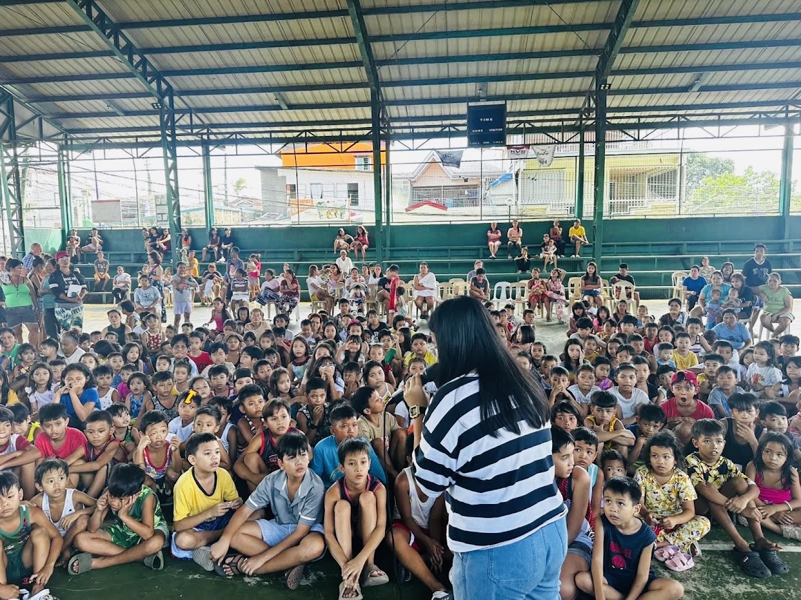 A young leader at the mic in front of the seated children.
