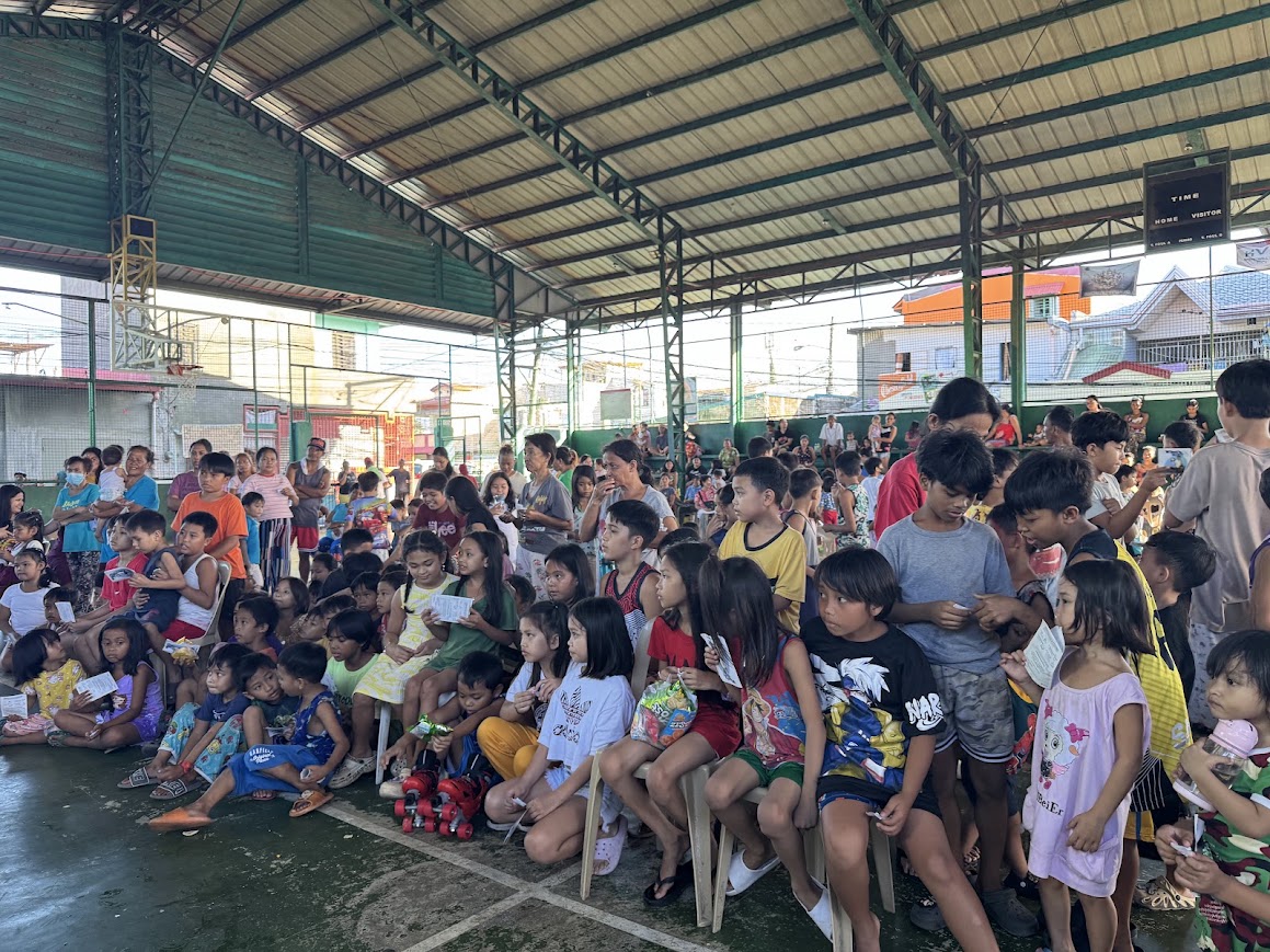 Children seated on the court with their snacks and pamphlets.